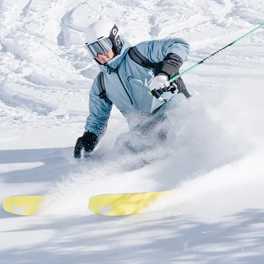 Skifahrer in blauem Anzug und mit weißen Helm beim Carven durch Pulverschnee.