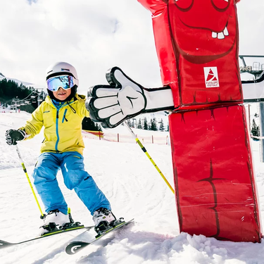 Ein Kind fährt fröhlich auf Skiern an einer roten Figur auf der Funslope Steffisalp vorbei.