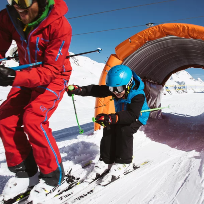 Zwei Skifahrer fahren durch einen schneebedeckten Tunnel auf der Kidscross-Strecke am Salober.