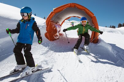 Zwei Kinder fahren beim Kidscross Salober durch einen Schneetunnel.