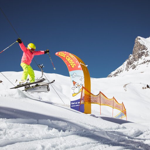 Skifahrer springt im Kidscross Salober bei Sonnenschein und über eine Kuppe.
