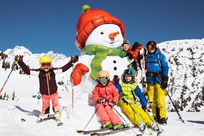 Familie posiert mit einem Schneemann beim Skifahren in den Bergen.