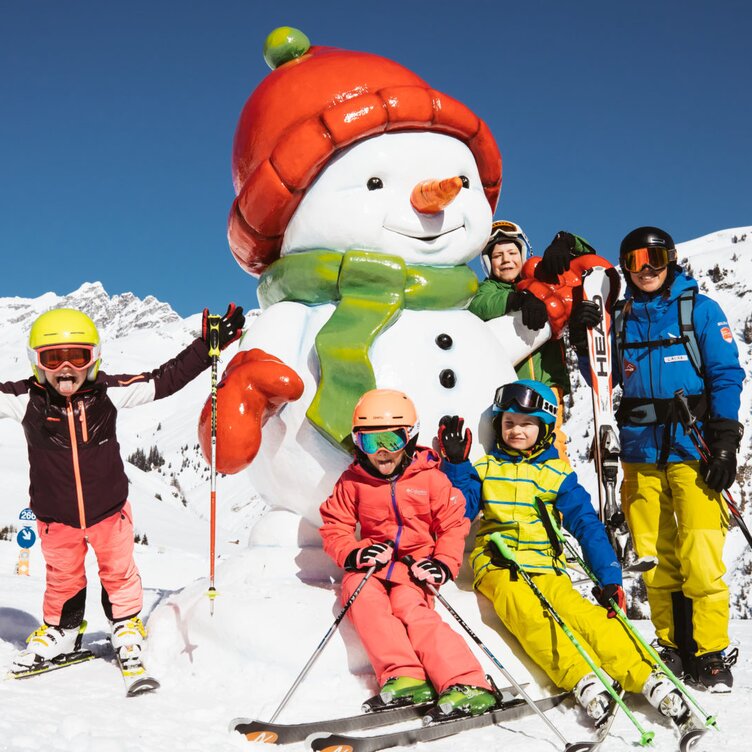 Familie posiert mit einem Schneemann beim Skifahren in den Bergen.