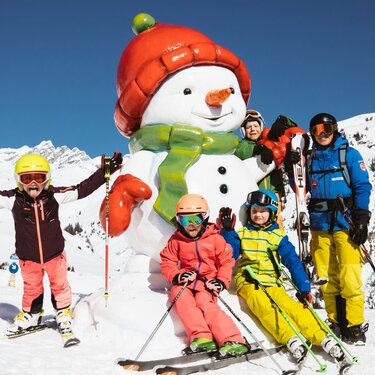 Familie posiert mit einem Schneemann beim Skifahren in den Bergen.