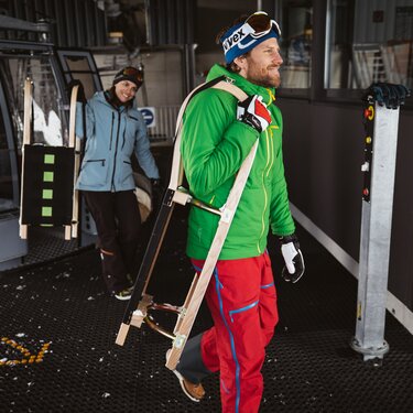 Zwei Personen steigen aus der Gondel aus und tragen die Rodeln zur Abfahrt.