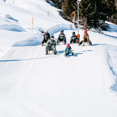 Five people sledding down a snow-covered track.