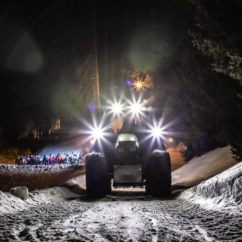 Traktor mit Scheinwerfern beleuchtet nächtliche Winterlandschaft.