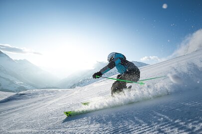 Skifahrer in Aktion auf schneebedecktem Hang bei sonnigem Wetter.