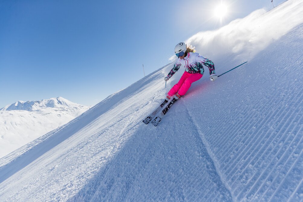 Skifahrerin mit pinker Skihose bei sonnigem Wetter auf einer Piste.