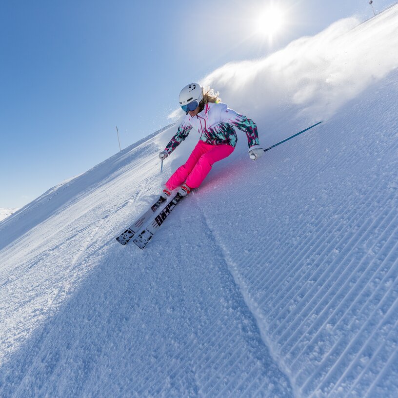 Skifahrerin mit pinker Skihose bei sonnigem Wetter auf einer Piste.