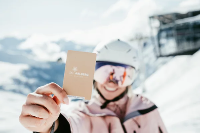 Person mit Skipass von Ski Arlberg vor schneebedeckter Landschaft.