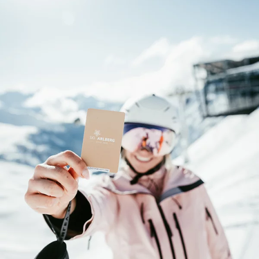 Person holding Ski Arlberg ski pass against snowy backdrop.