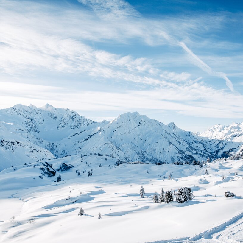 Panorama der verschneiten Berge in der Skiregion Warth-Schröcken mit blauem Himmel und Wolken.
