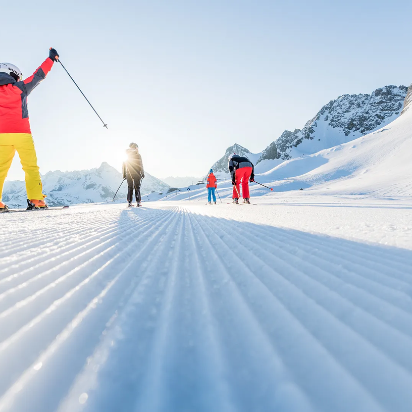 Menschen beim Skifahren auf einer präparierten Piste an einem sonnigen Tag.