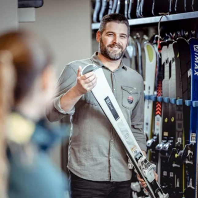 Ein Verkäufer zeigt einer Kundin Ski in einem Skiausrüstungsgeschäft.