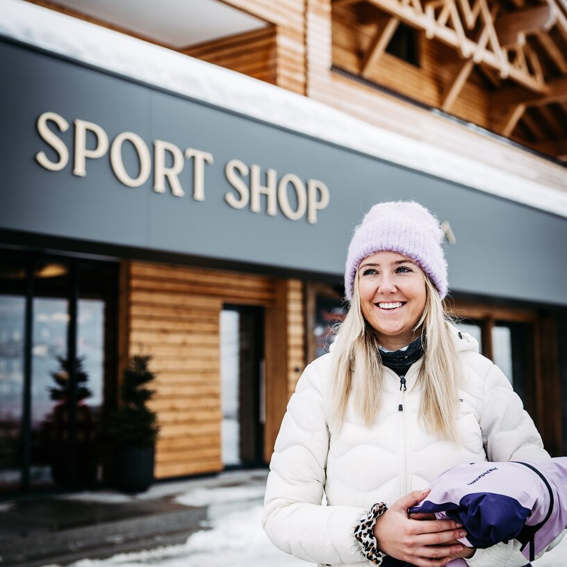 Eine lächelnde Frau in Winterkleidung steht vor einem Sportgeschäft.