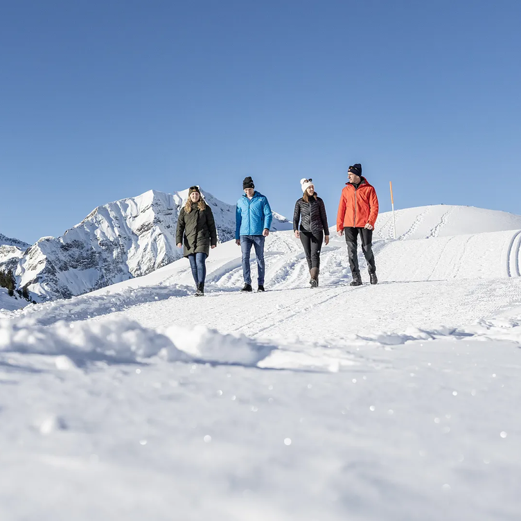 Vier Personen wandern durch die schneebedeckte Berglandschaft am Arlberg.
