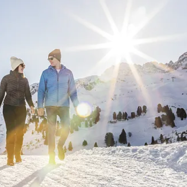 Two people hiking through snowy mountains in the sunshine.